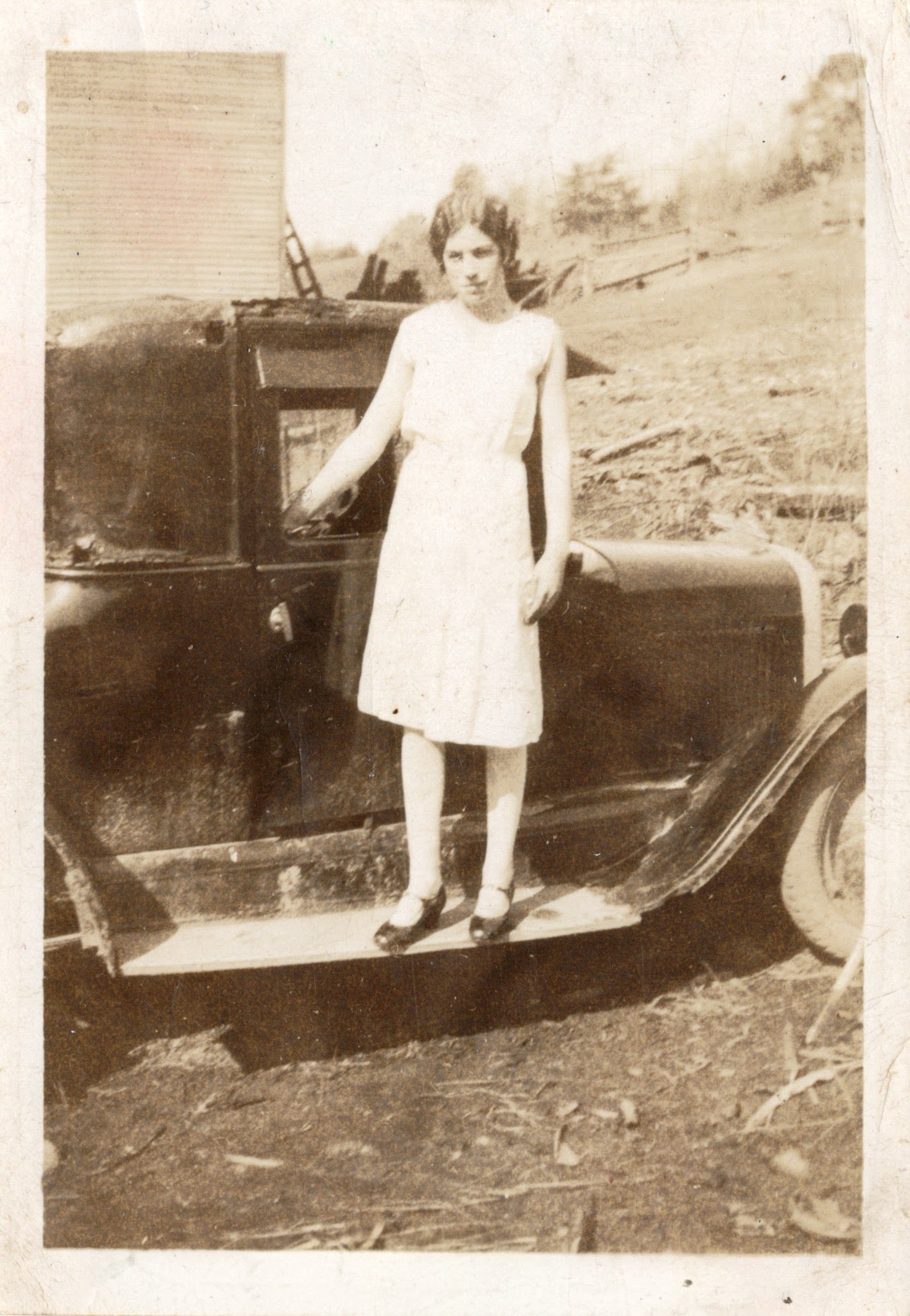 Woman in a white dress standing next to an old car outdoors